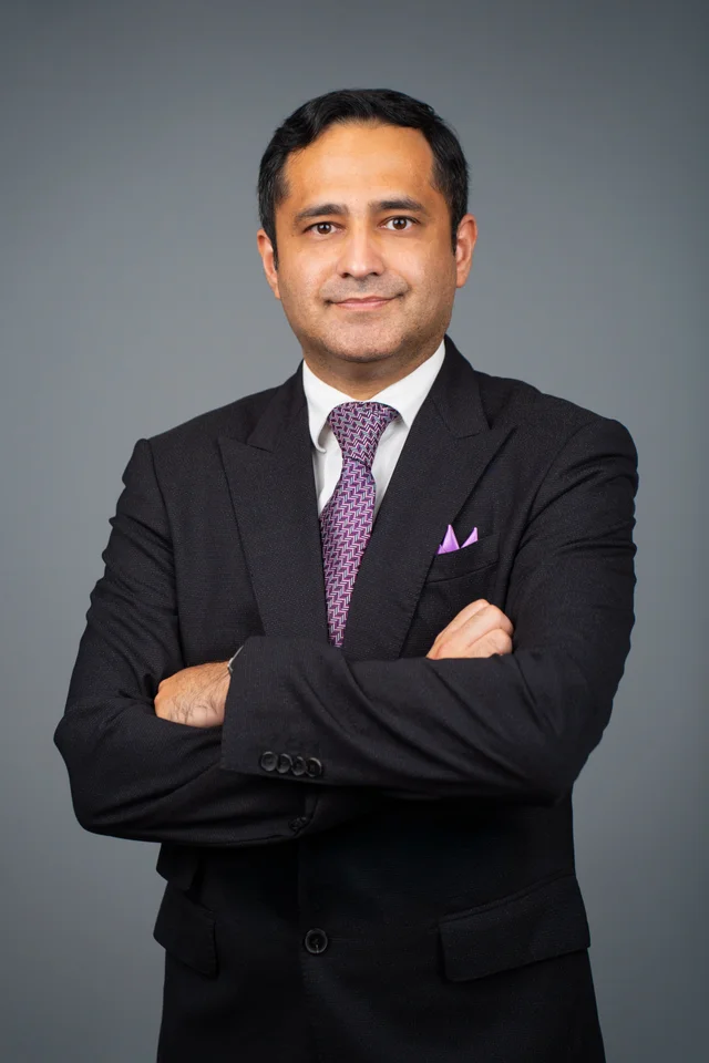 Zahaib Nabeel in a dark suit, photographed against a grey studio background.