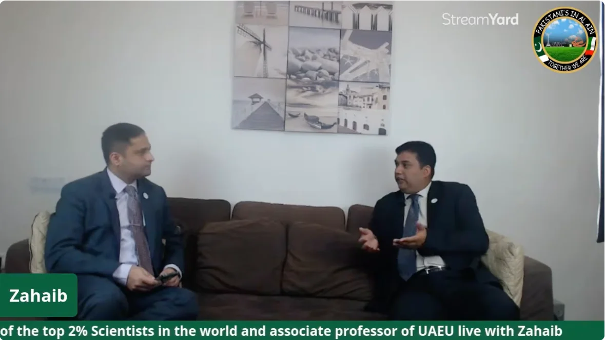 Two men seated on a sofa in conversation during a live interview for the Pakistanis in Al Ain community, with the group logo in the corner of the frame.